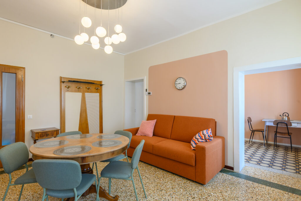 Vista completa su salotto con tavolo rotondo e quattro sedie, divano letto. Soggiorno retrò stile anni 70.