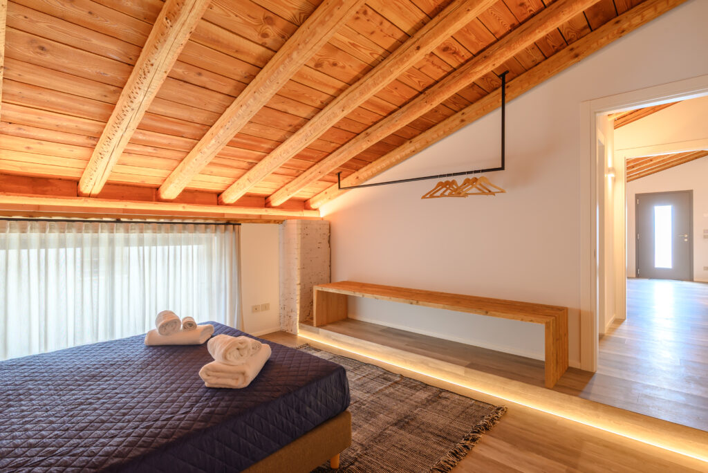 Zona open space per vestiario davanti a letto matrimoniale in ambiente rustico e moderno con soffitto a travatura